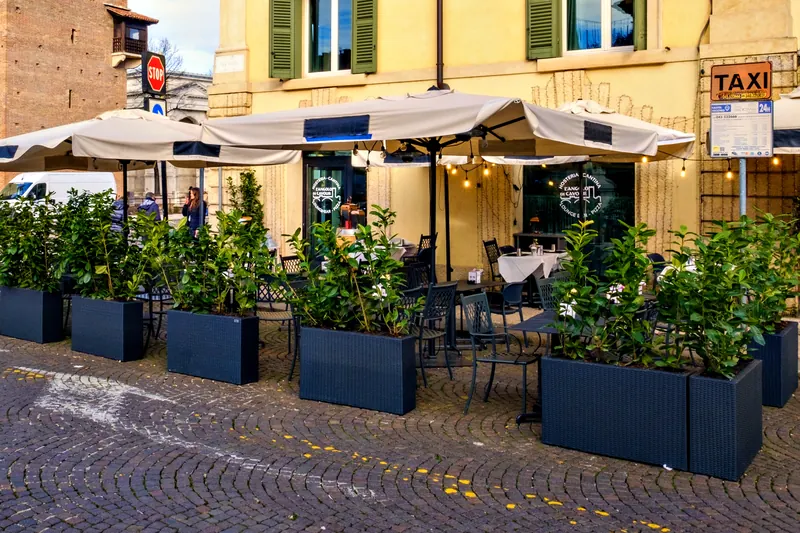 罗马路黄色外墙前摆放阳伞和绿植的露天座位 – L'Angolo di Cavour，维罗纳
