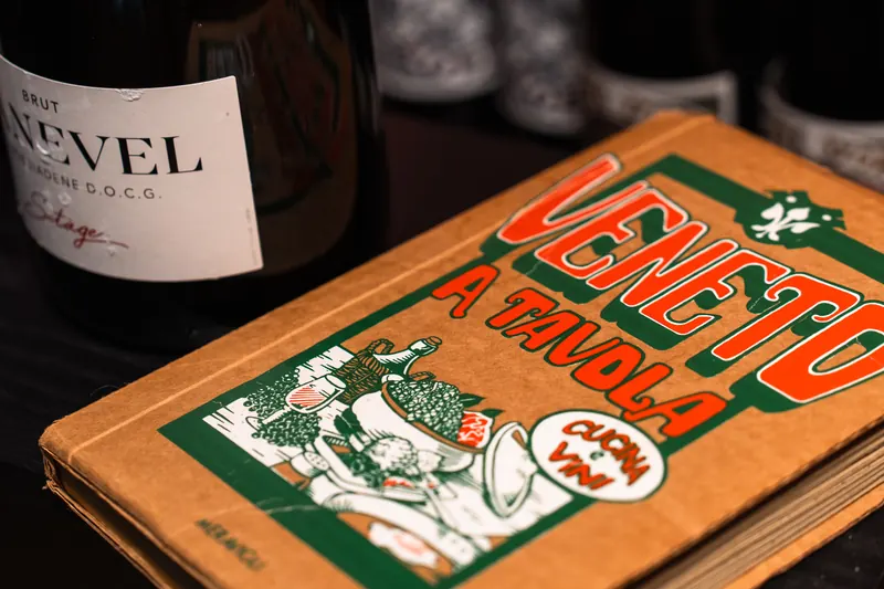 一瓶瓦尔多比亚德内起泡酒，旁边是《Veneto a tavola》一书 – L'Angolo di Cavour，维罗纳